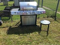 Front view of the stainless steel Grill Chef propane BBQ with side burner to the right and metal patio side table to the right of the BBQ.