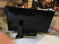 Front view of RCA flat screen TV on stand with remote control on stand and Toshiba Dynadock in front.