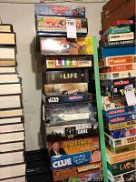 Stack of vintage and themed board games showing front and side of boxes including Monopoly editions, Puzz 3D, The Game of Life, Lord of the Rings, Star Wars Operation, Walking Dead Trivia Game, Trump The Game, Clue, and others.