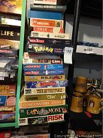 Stacked vintage board games and puzzles including Monopoly, Pokemon Master Trainer, Bibleopoly, Clue, and others, showing well used condition.