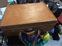Full view of the vintage leather suitcase with straps, showing the medium brown leather surface and rectangular shape.