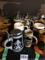 Group of 8 vintage hand painted ceramic beer steins displayed together showing various designs and pewter lids