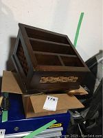 Wooden organizer with several compartments, placed on cardboard boxes and other items.