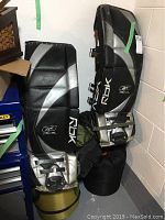 Overall view of the two RBK goalie pads standing upright against a wall, showing black and silver color and visible signs of heavy use.