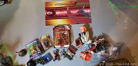 Full view of lot with various toys and collectibles including boxed action figures, loose figures and cards on a table surface.