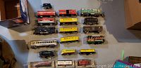 Top view of multiple unboxed vintage model train cars arranged on floor. Variety of freight cars, passenger cars, and tank cars from Marx and Lionel brands.