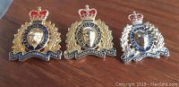 Three Royal Canadian Mounted Police pins, gold with blue and red enamel, and a profile of a mounted officer