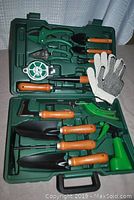 Complete gardening tool set arranged inside a green hard carrying case, showing all tools and gloves.