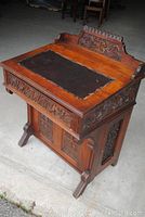 Front angled view showing carved motifs on cornice, leather writing surface and foot design