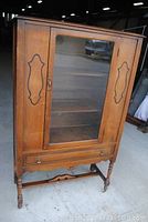Full view of the antique walnut china cabinet showing the glass door with wooden decorative panels, bottom drawer with brass pulls, and castor wheels.