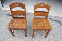 Pair of two vintage solid oak wood church chairs with carved trefoil motifs and shelves for hymnals visible, sitting on pavement.