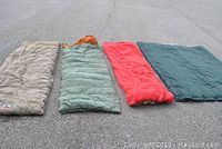 Four sleeping bags laid out flat outdoors showing full length and colors (beige, green with orange, red, dark green)