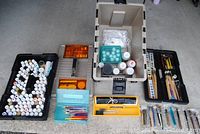 Full overview of art supplies including paint bottles, brushes, palettes, and case compartments laid out for display.