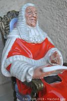 Close-up photo showing the upper body and details of the judge figurine, including the facial expression and hand gestures holding papers.