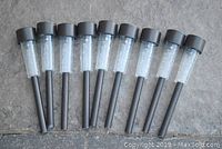 Nine garden solar lights laid out on concrete, showing top diffuser and black stakes.