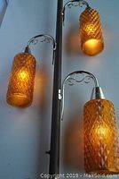 Close-up showing three amber glass light pendants with warm illumination and decorative scroll metal arms attached to dark metal pole.