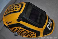 Yellow and black Miller-CAT digital elite series welder's helmet shown angled from the side, displaying front and top with honeycomb pattern and large viewing window.