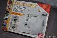 Boxed Dressmaker Sewing Center featuring 100-piece accessory kit highlighted on packaging. Box shows product features including sewing from silk to denim, horizontal drop-in bobbin, and pre-threaded ready to use machine.