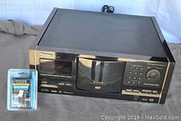 Front and top angled view of black Pioneer DV-F07 DVD player with disc carousel and control buttons, placed on grey surface next to packaged RCA splitter.