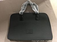 Front view of black travel bag with plastic-covered handles and logo patch.