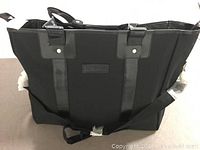 Front view of black ladies travel bag showing fabric and shiny trim with handles and shoulder strap.