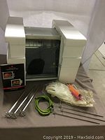 Full view of the Showtime Rotisserie & BBQ unit with accessories laid out in front: skewers, gloves, handles, and manual, with original foam packaging on sides.