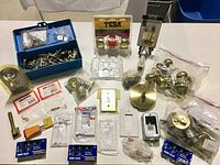 Full view of hardware laid out showing Tesa and Taymor packaging, blue toolbox with loose hardware, various brass knobs, wall plates and other electrical accessories.