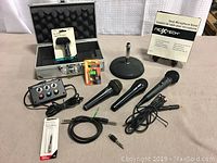 Full lot overview showing carrying case, microphones, cables, mic holder, mic stands, connector box, and other accessories arranged on a flat soft surface.