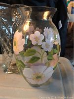 Vase with hand-painted white and light purple flowers and green leaves on clear glass, showing floral design and shape.