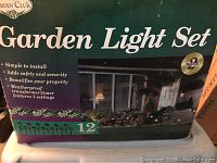 Box packaging showing Garden Light Set with features listed: simple to install, adds safety and security, beautifies property, weatherproof transformer with 3 settings, 12 lights included.