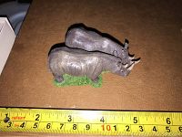 Photo of two rhino figurines standing on a green base with measuring tape showing about 3 inches length.