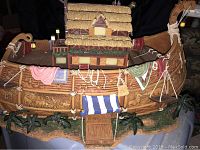 Detailed side view of Noah's Ark figurine from the Masterpiece Edition Hawthorne Village by Thomas Kinkade showing carved animal patterns, decorative cloth, ropes, and barn house on the ark.