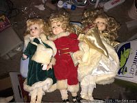 Three porcelain Christmas dolls lying side by side, showing full outfits and hair styles