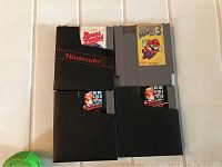 Three NES game cartridges including Super Mario Bros 3, with two original black Nintendo holders against white background.