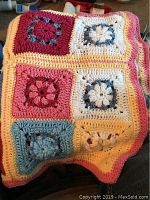 Close-up of a crocheted baby afghan blanket featuring multicolored squares in pink, blue, yellow, and white yarn, folded on a surface.