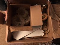 Box with white ceiling fan blades, clear flower-shaped glass light shades, brass motor housing and mounting hardware packed inside.