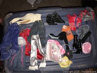 Photo of assorted Barbie doll clothes and accessories laid out in a plastic container: pants, skirts, tops, jackets, dresses, boots, handbags, and hats.