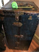 Photo of the upright steamer trunk showing metal reinforced edges, leather trim, and a measuring tape displaying approximate height of 36 inches.