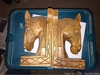 Pair of carved wooden horse head bookends placed side by side on a blue plastic container lid.