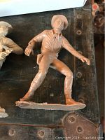 Light brown plastic cowboy figurine shown from a side angle on a dark surface