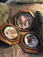 Three octagonal wooden framed decorative plates with Christmas scenes displayed on a couch