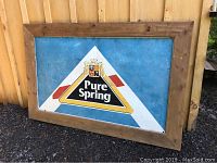 Full frontal view of the Pure Spring tin sign mounted in wood frame leaning against siding