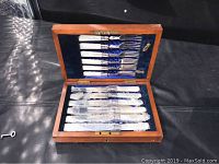 Open wooden box displaying the mother of pearl handled forks and knives wrapped in plastic.