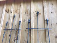Two steel garden trellises leaning against a wooden fence, each with three Fleur de Lis decorative tops.