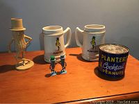 Overall view of two ceramic Planters beer mugs, vintage tin can of Planters Cocktail Peanuts, Planters Guy salt and pepper shakers, and a peanut-shaped bank figure.