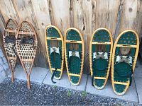 All three pairs of snowshoes displayed against a wooden fence; one vintage wooden pair to the left, two pairs of yellow-framed Faber Winter Hiker snowshoes to right.