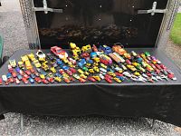 Wide view of the large assortment of mini toy cars and trucks spread on a black surface showing many rows and different types, colors, and makes.