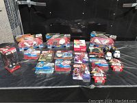 Wide shot of 20 pieces of Star Wars collectables in unopened packages displayed on a black cloth. Items include Hot Wheels vehicles, boxed vinyl bobble head, action figures, and other blister packaged figures.