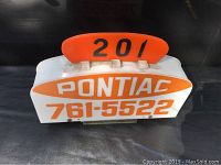 Front view of vintage taxi roof sign showing orange and white 'Pontiac' with phone number 761-5522 and number panel 201 in orange on top.