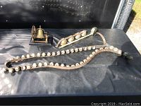 Three bell pieces: a brass desk bell on a wooden base, a metal bar with four mounted brass bells, and a leather belt with multiple small bells.